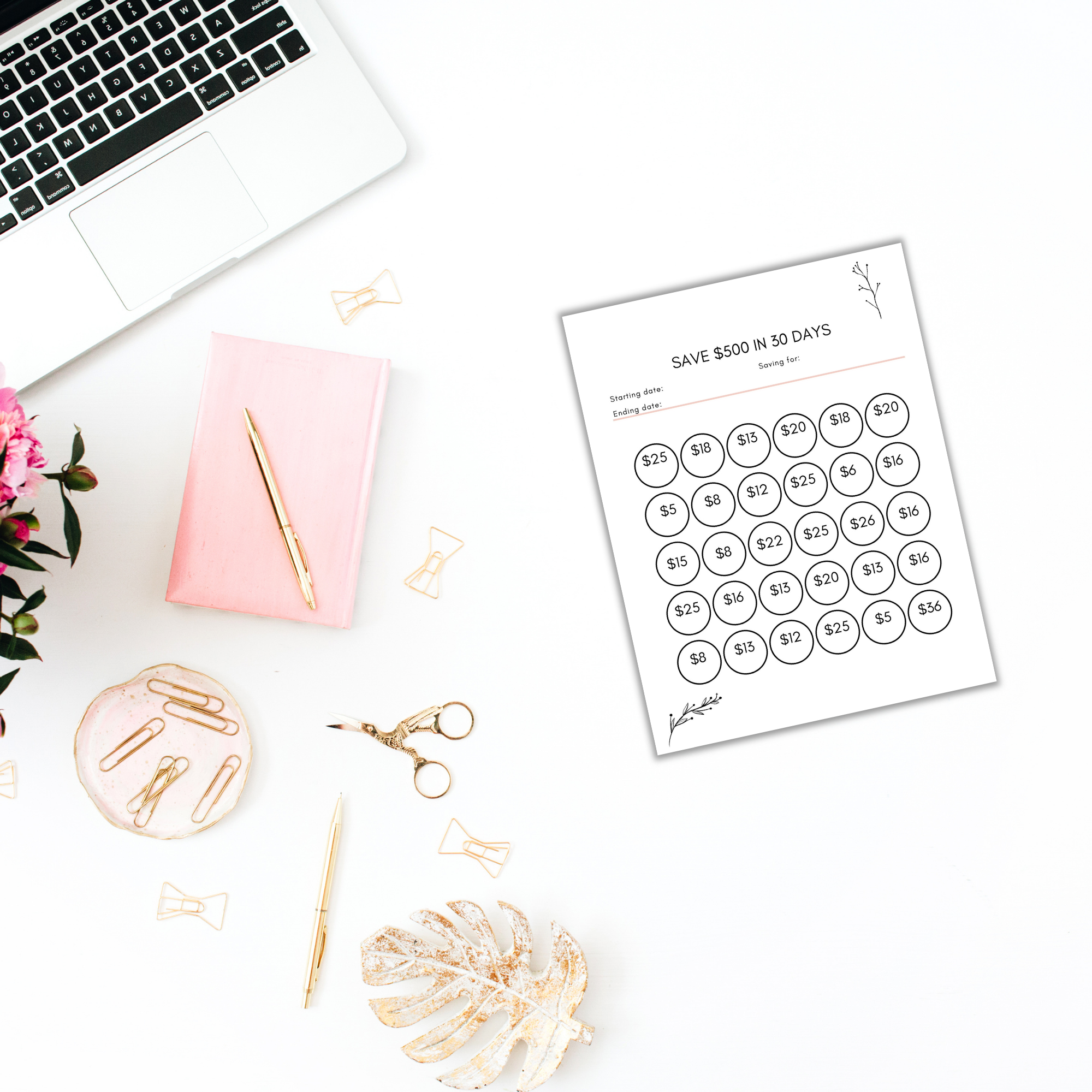 A desk with a laptop, pink notebook, pen, scissors, paperclips, flowers, and "The 100 Envelope Challenge" tracker template sits ready for action.