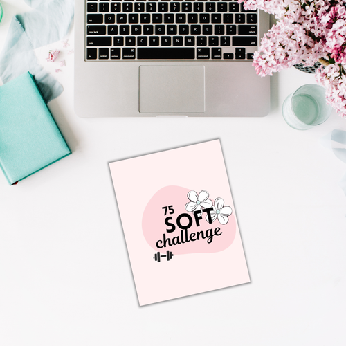 A laptop, open notebook, and vibrant flowers are neatly arranged on a white table alongside 'The 75 Soft Challenge' Trackers booklet with handy organizers.