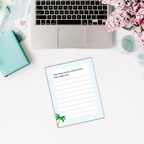 An open laptop rests on a white desk adorned with pink flowers, a turquoise book, and a sheet titled "I had a dream recently, and here's what I think it might mean..."—the perfect setting for jotting down thoughts in your Summer Journal for Kids.