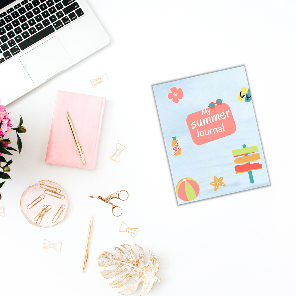 Flat lay featuring the Summer Journal for Kids, positioned next to a laptop, pink notebook, gold stationery, scissors, and flowers on a white surface.