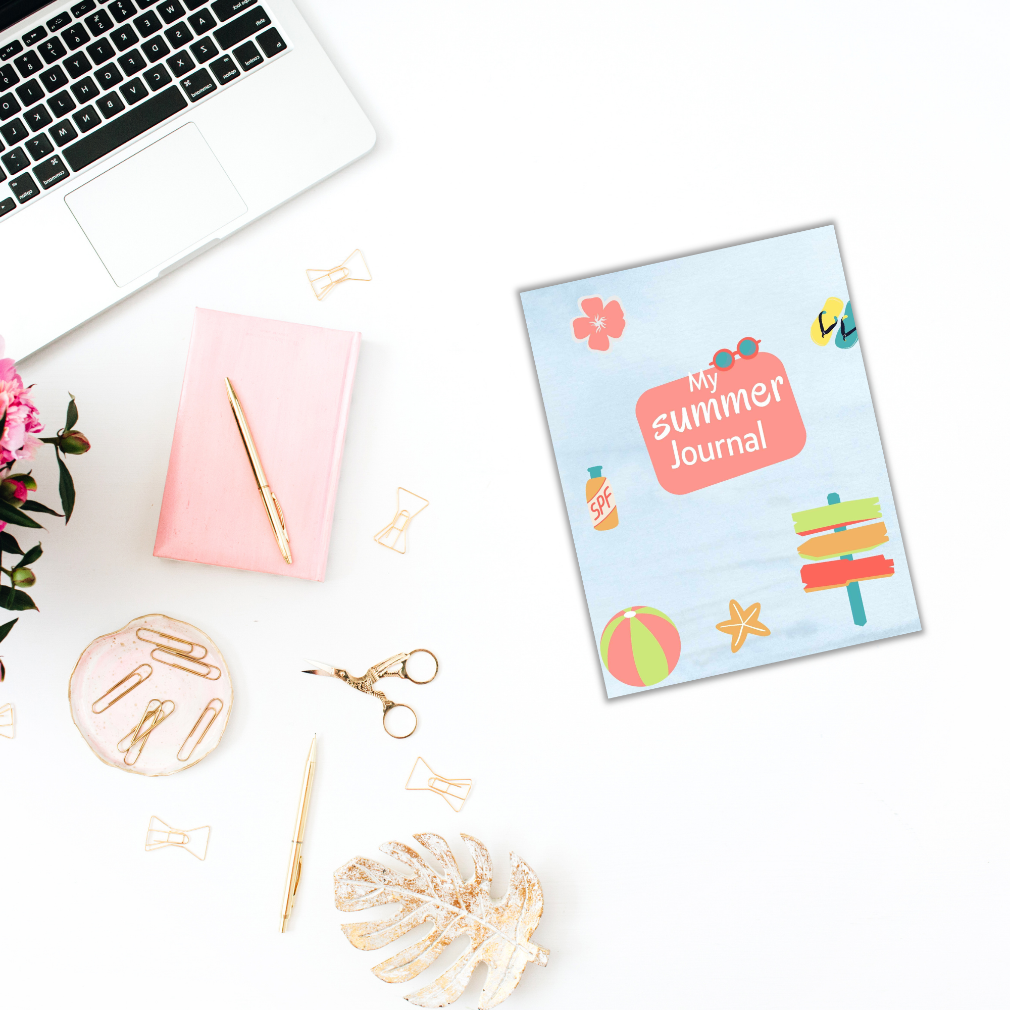 Flat lay featuring the Summer Journal for Kids, positioned next to a laptop, pink notebook, gold stationery, scissors, and flowers on a white surface.