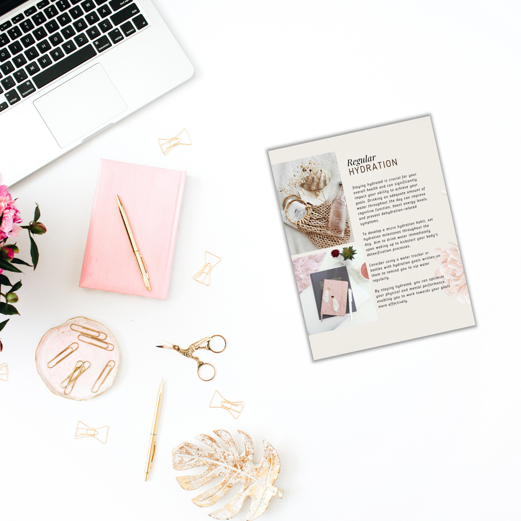 Aerial view of a workspace featuring a laptop, the "Powerful Micro Habits - Ebook & Workbook," a pink notebook, and a gold pen laid next to the open ebook. Scissors, a magazine, and decorative items like pink flowers, a palm leaf, and scattered gold paperclips complete the scene on a crisp white background.