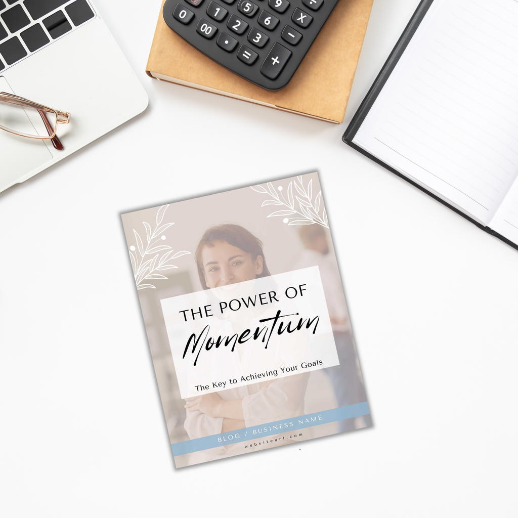 Flat lay of a magazine titled "The Power of Momentum" on a desk with The Power of Momentum Journal & Workbook, calculator, glasses, and a pen.