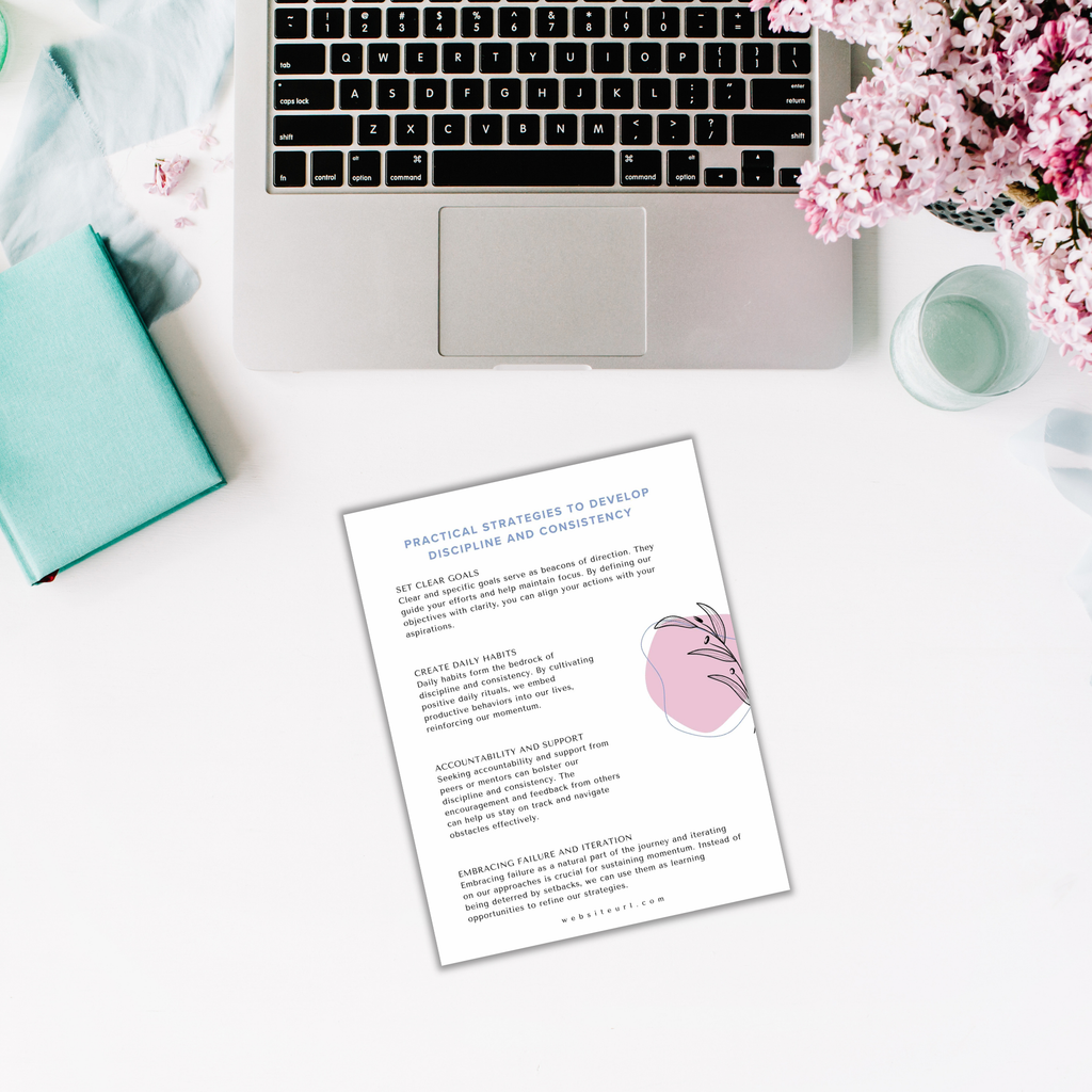 A laptop on a white desk surrounded by pink flowers, a turquoise book, and a cup sits next to The Power of Momentum Journal & Workbook alongside a printed sheet titled "Practical Strategies to Develop Discipline and Consistency.