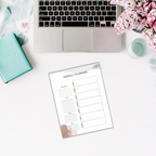 Overhead view of a laptop, a closed book, flowers, a candle, and the Productivity Planner Templates on a white desk.