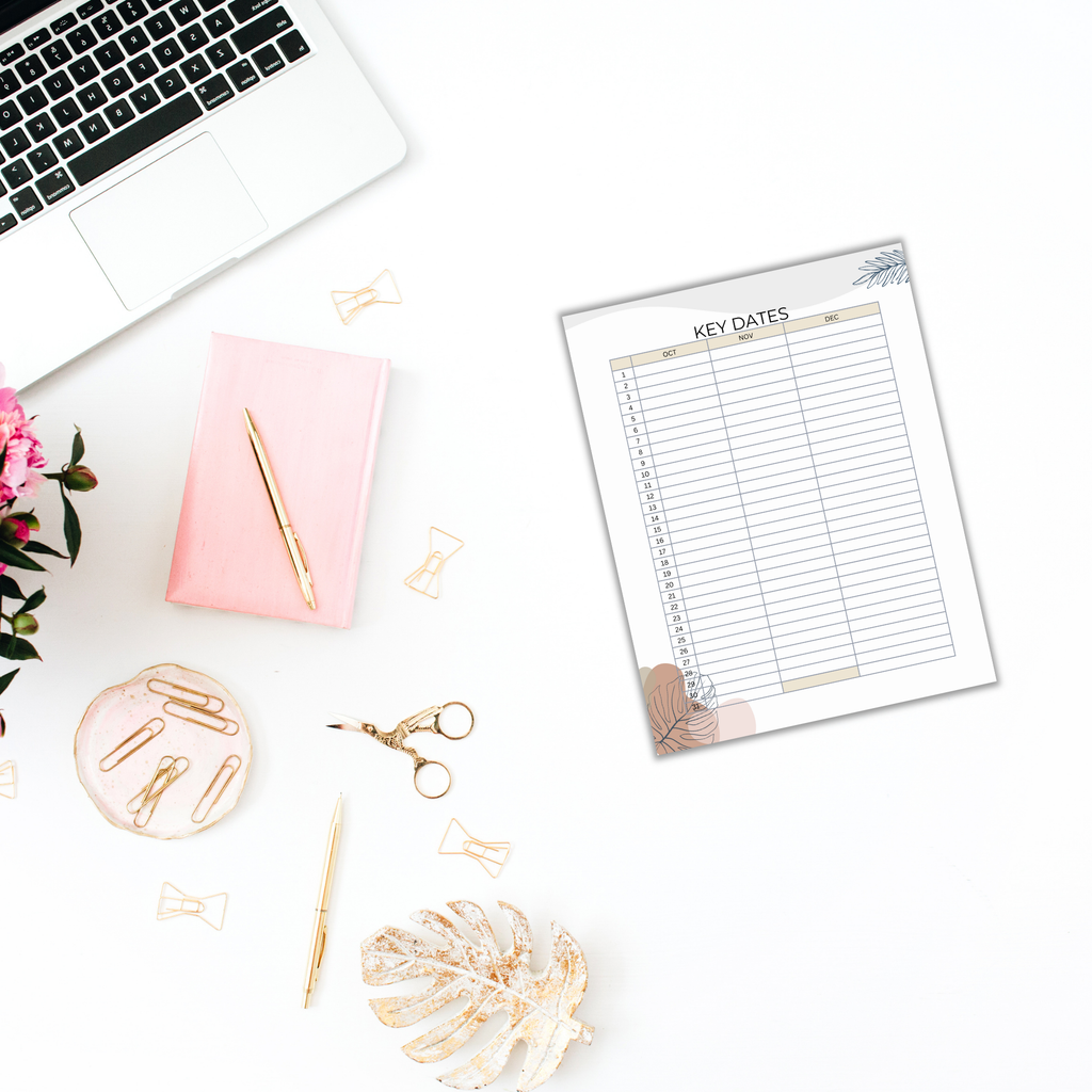 A laptop, notebook, pen, and a key dates planner sit on a white desk, surrounded by flowers, paper clips, and scissors—creating a perfect workspace for productivity. With Productivity Planner Templates at hand, it's an ideal setup to plan and organize efficiently.