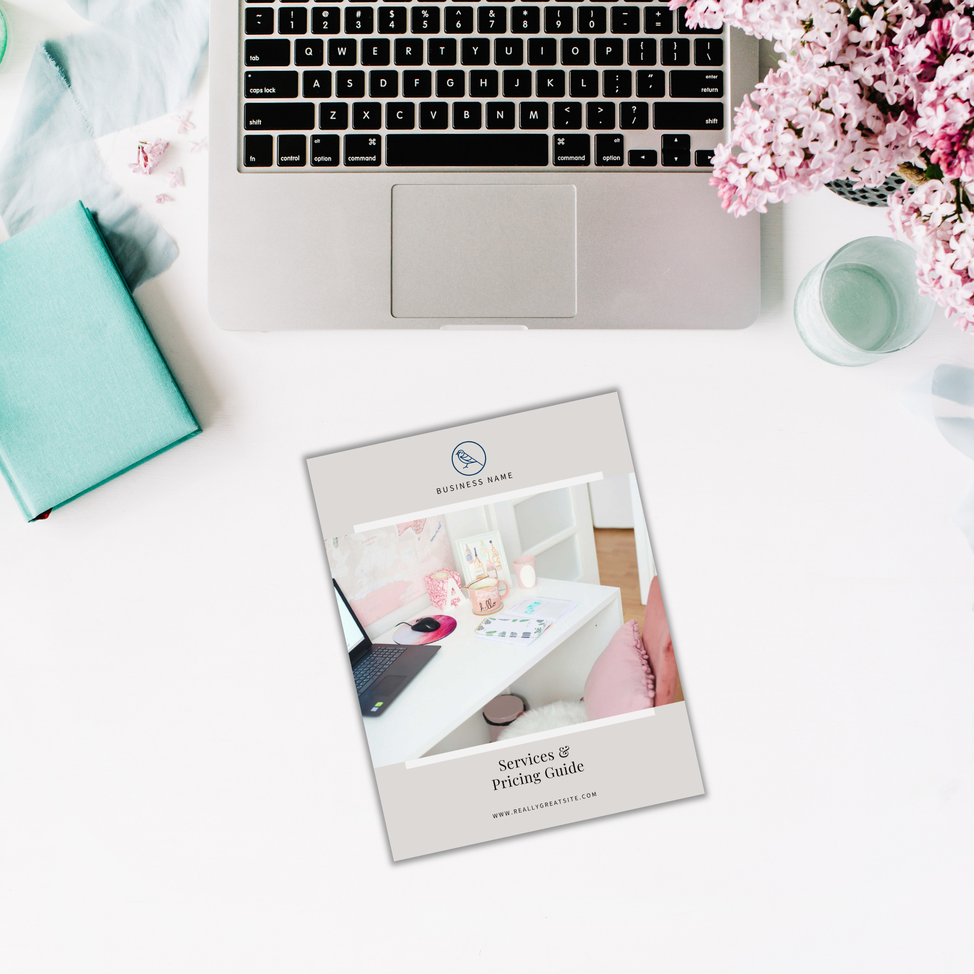 Open laptop on a table with a teal book, the Services and Pricing Guide featuring a floral cover, a candle, and pink flowers nearby.