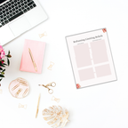 A workspace creatively arranged from a top-down perspective showcases a laptop, a pink notebook, a pen, paper clips, and scissors. Also visible is a sheet titled "Reframing Limiting Beliefs." Positioned nearby is the Vision Board Bundle filled with inspiring images. The setting is further enhanced by the presence of a pink flower and decorative leaf adding charm to the composition.
